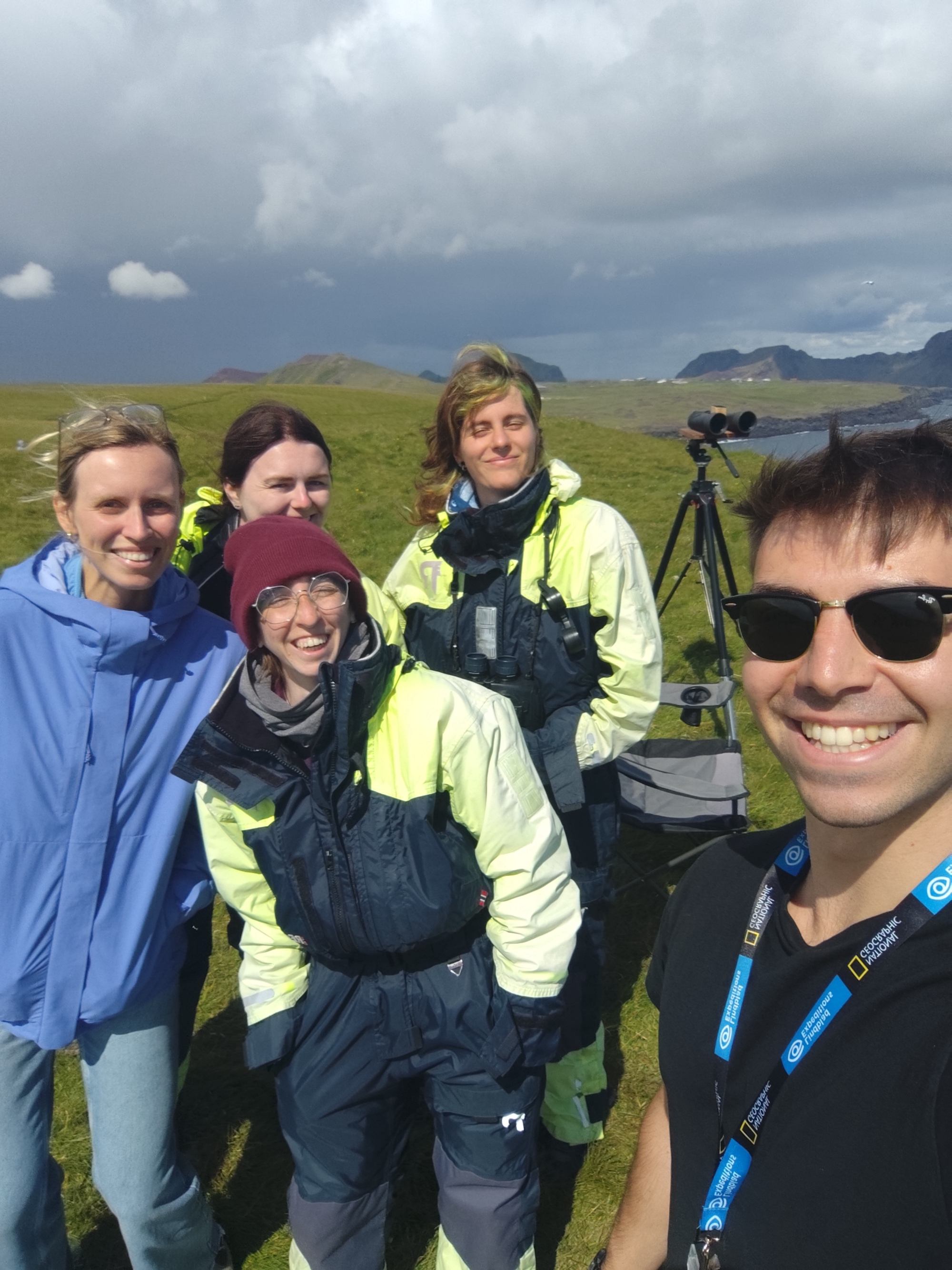 A group of five researchers posing for a selfie outdoors in Iceland, wearing outdoor gear, with a scenic landscape in the background.